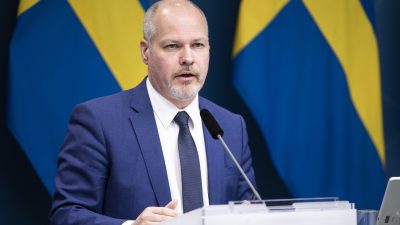 justitie- och inrikesministern Morgan Johansson håller ett tal framför två svenska flaggor.